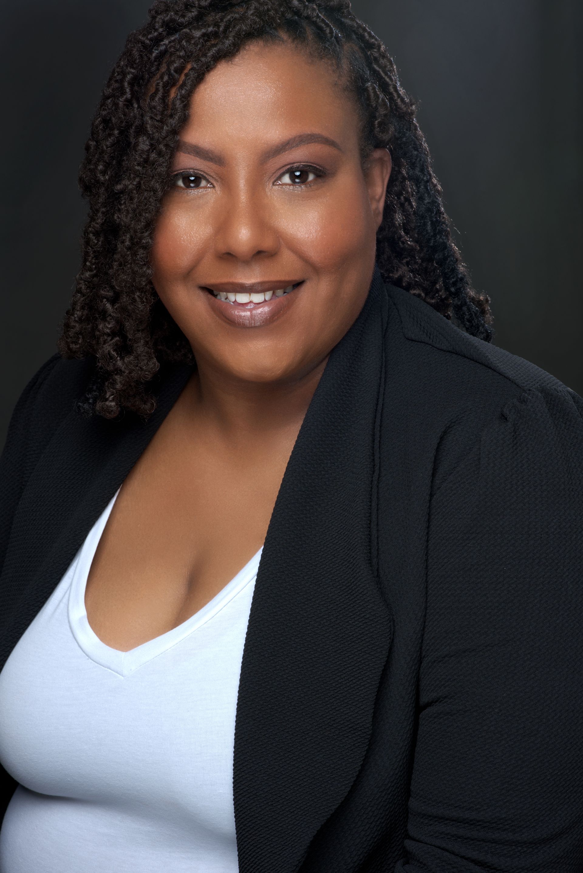 Portrait of a smiling person in a black blazer and white top against a dark background