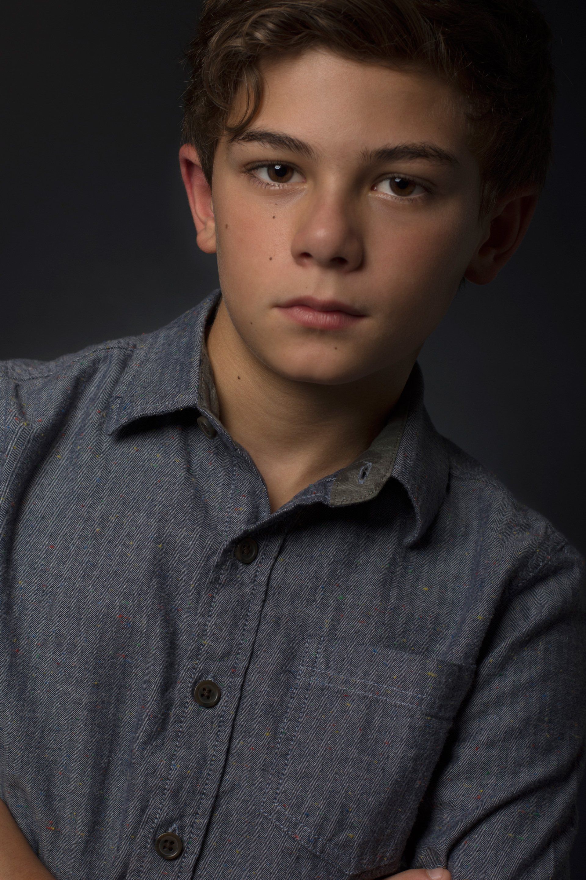 Portrait of a young person in a gray patterned shirt against a dark studio background