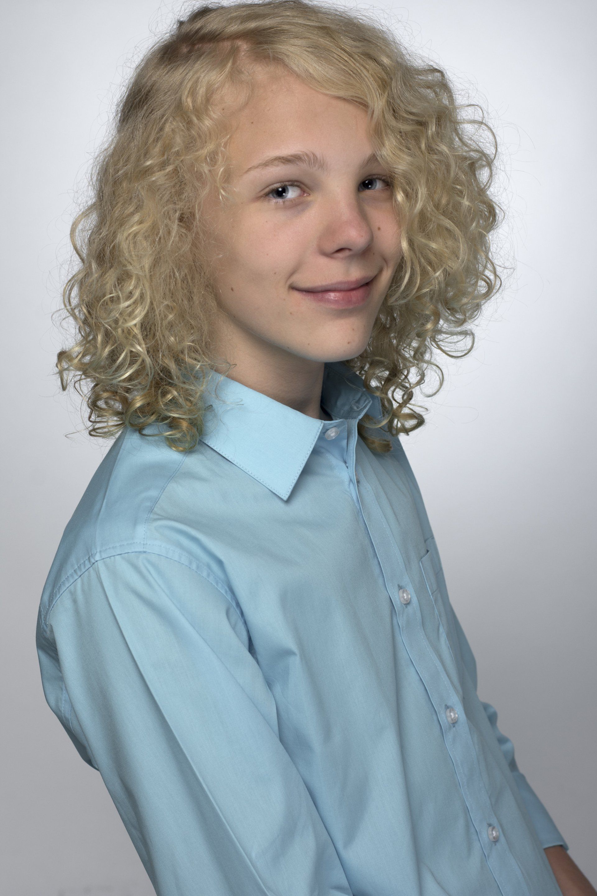Portrait of a person with curly blonde hair wearing a light blue shirt against a gray background