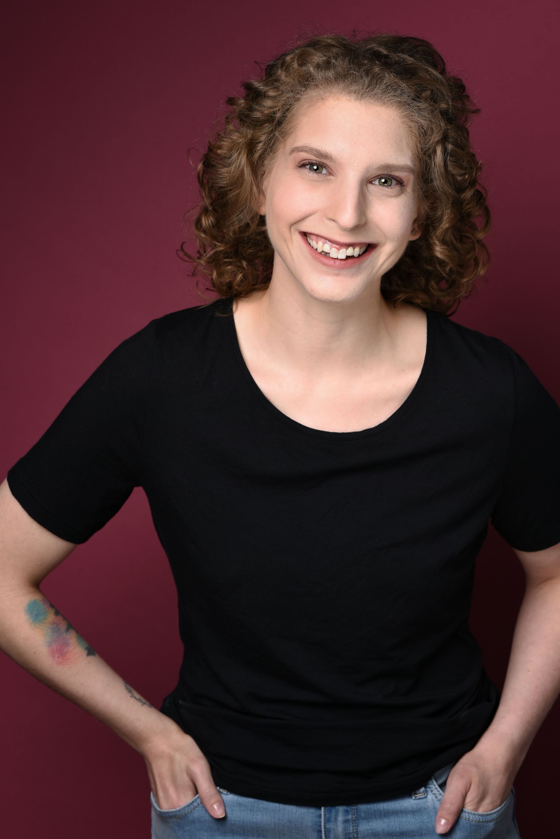 Smiling person in a black shirt and jeans against a burgundy background