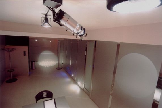 Stanza scarsamente illuminata con faretto a soffitto e luce circolare sulla parete, vista dall'alto.