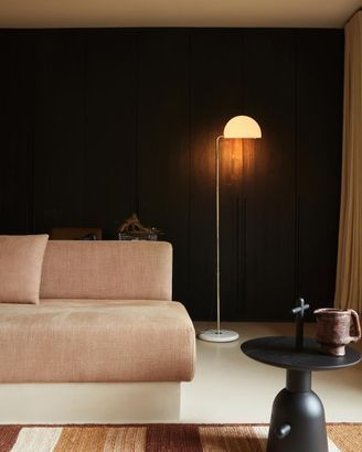 Soggiorno moderno con divano beige, parete nera, lampada da terra e tavolino rotondo.