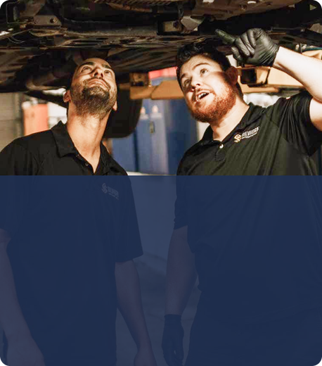 Two men are working under a car in a garage. | Silvhorn Automotive