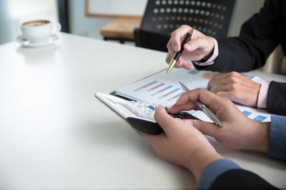 A Man and a Woman Are Sitting at a Table Looking at a Calculator — Optimus 1 Insurance Brokers in Westcourt, QLD
