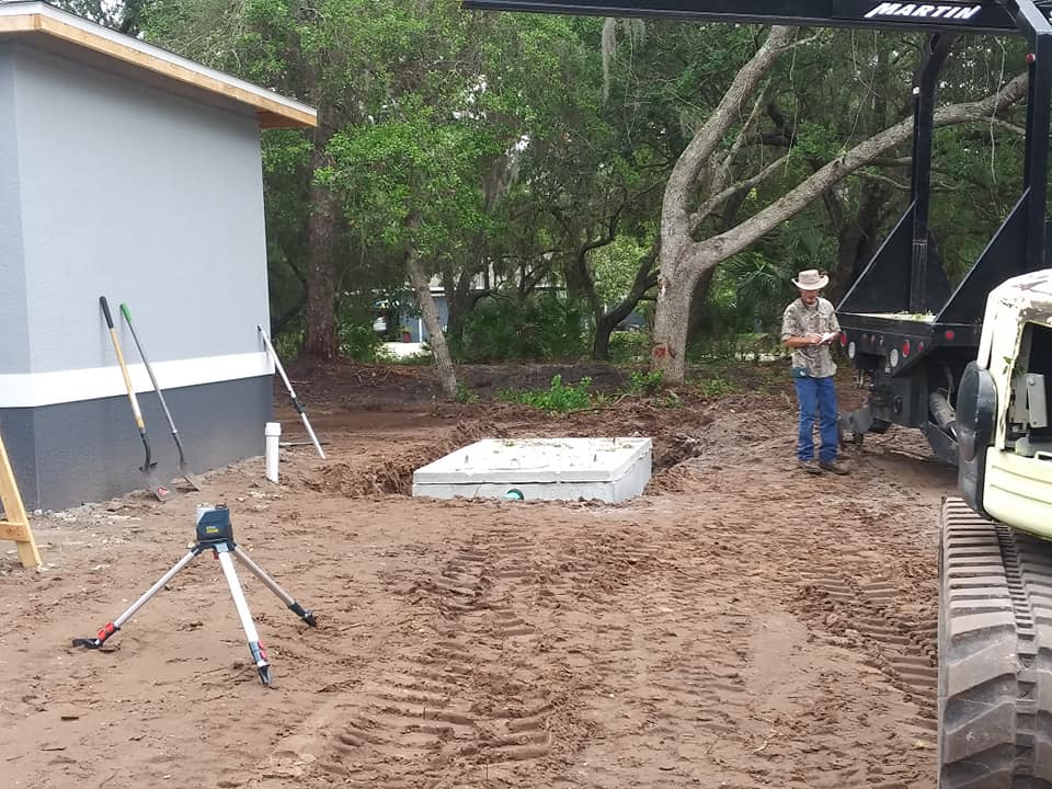 Construction site with dirt ground, tripod, concrete slab, and a worker near an excavator
