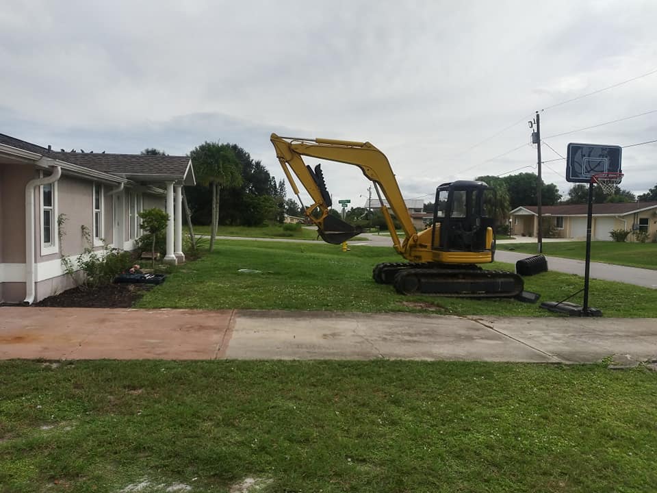 Yellow excavator parked on a lawn beside a house and driveway in a suburban neighborhood