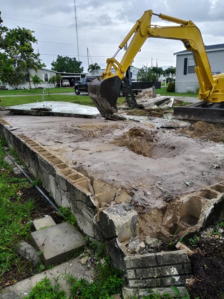 Yellow excavator tearing up a demolished concrete slab in a residential yard