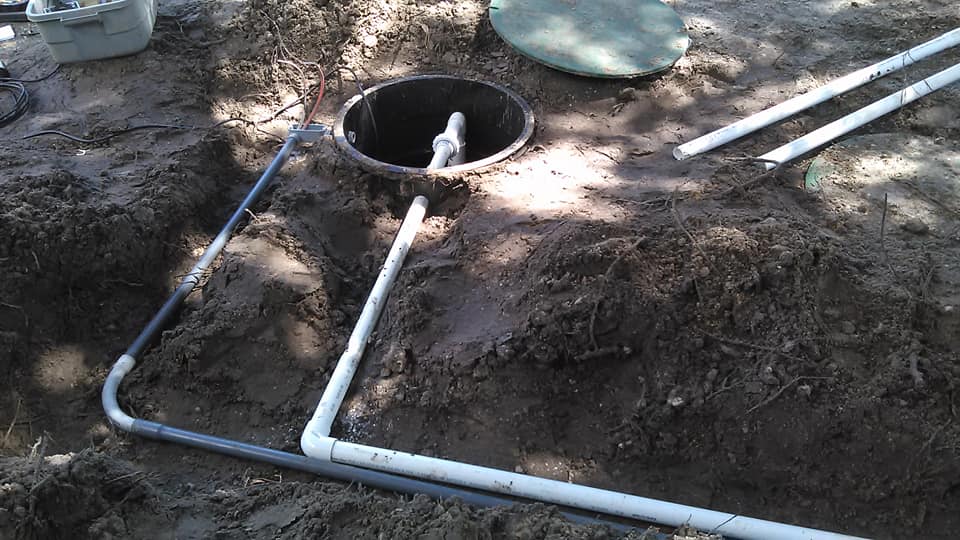 PVC pipes around a round septic tank opening in a dirt excavation site