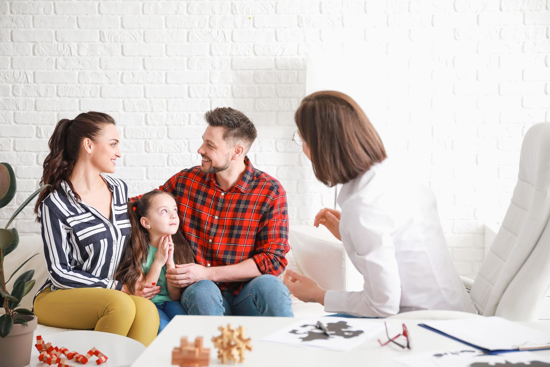 Family of three sitting with a healthcare professional, possibly a therapist; white room setting.