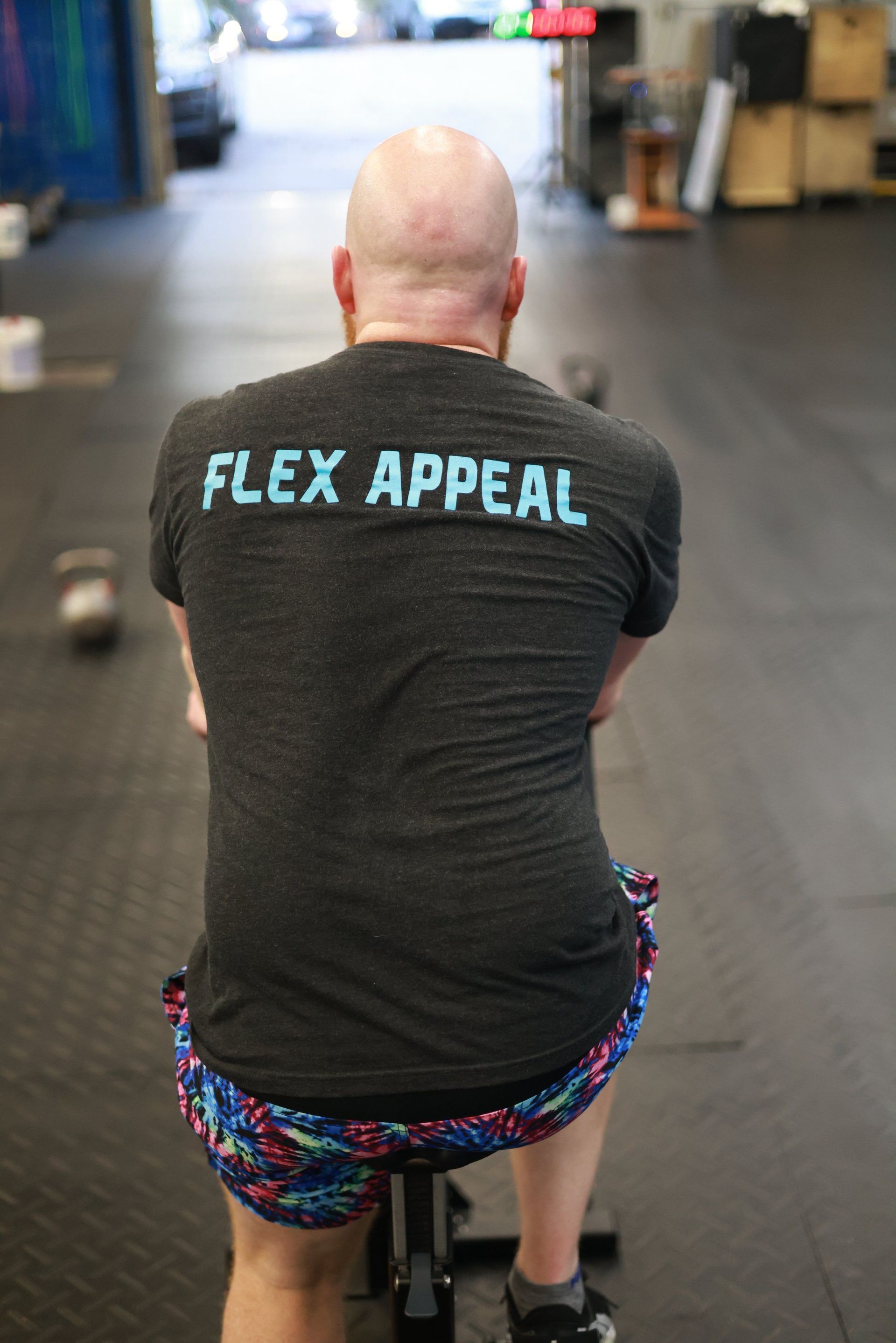 A man is sitting on a rowing machine in a gym wearing a flex appeal t-shirt.
