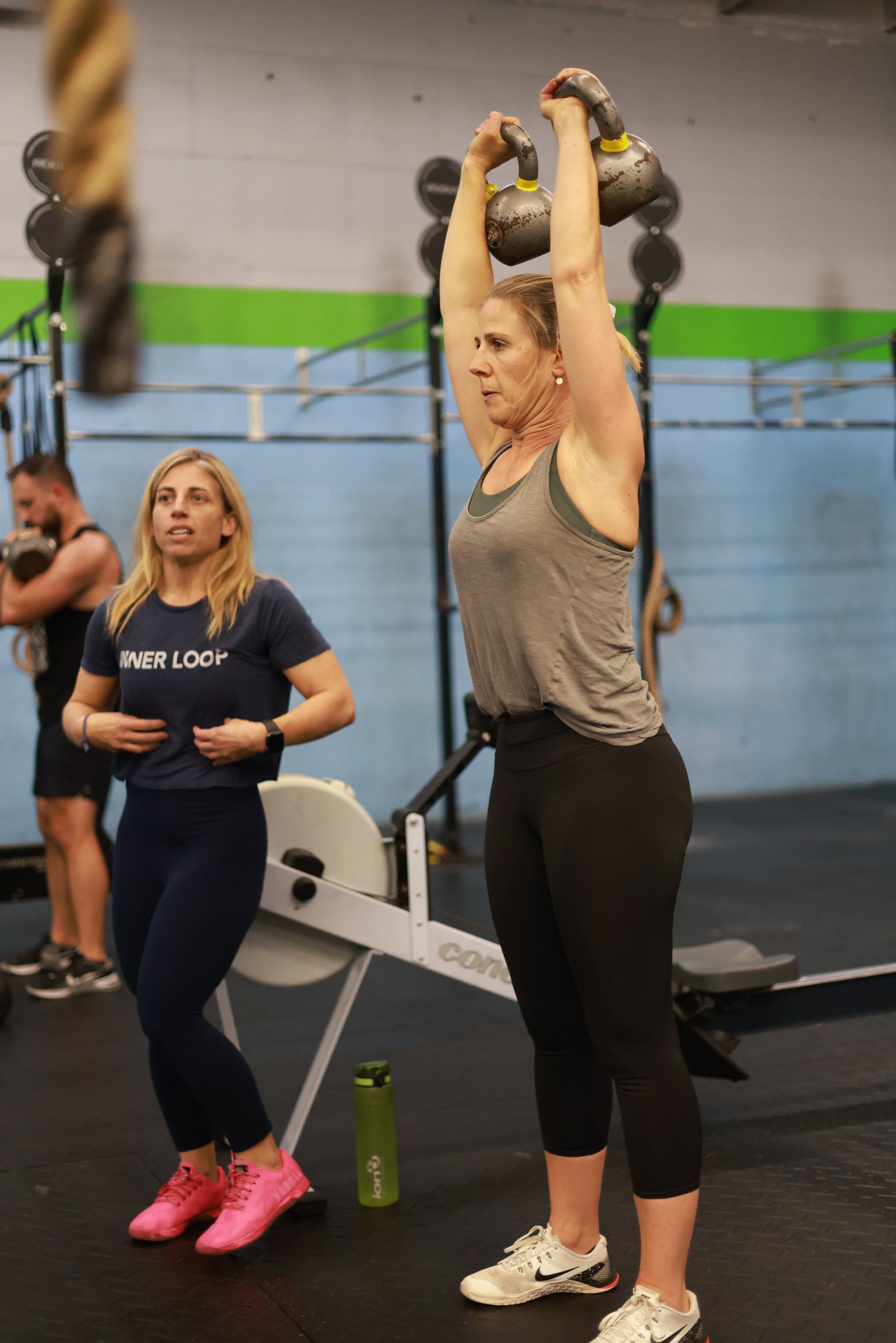 A woman is lifting a kettlebell over her head in a gym.