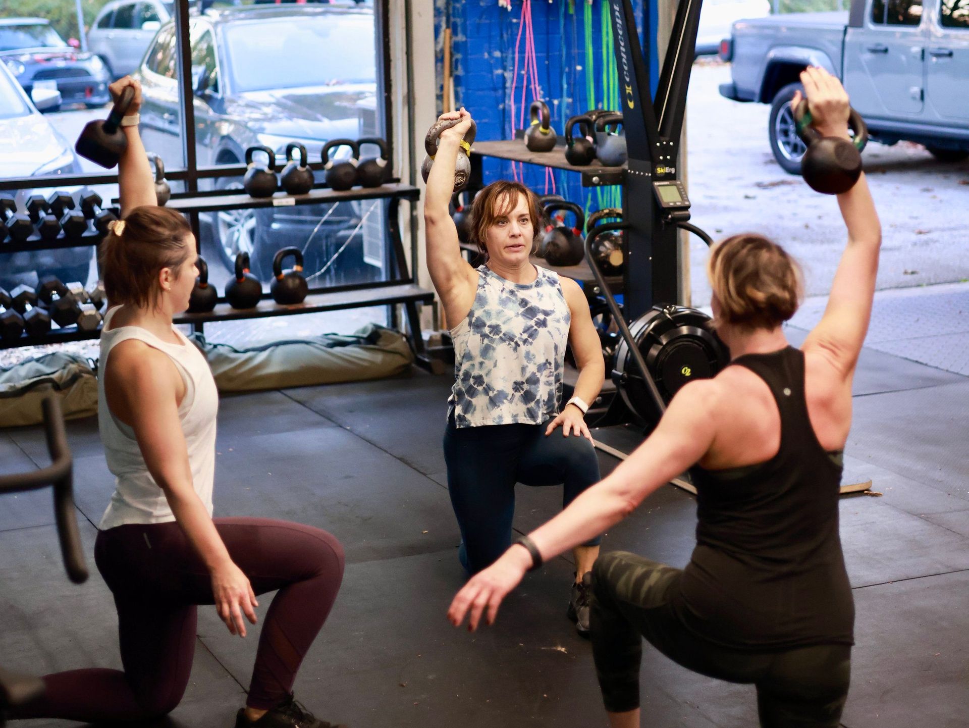 Three women are doing lunges with kettlebells in a gym.