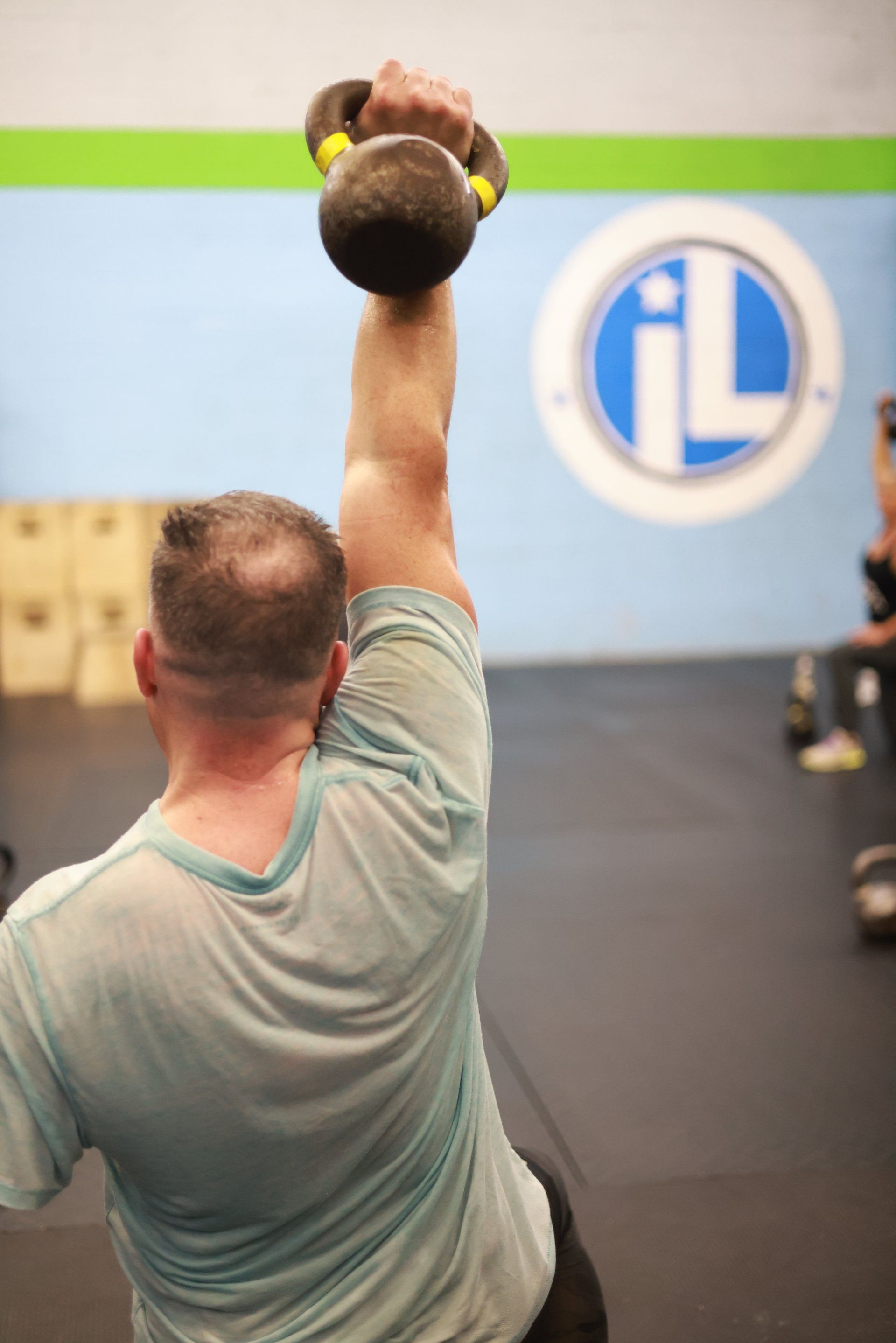 A man is lifting a kettlebell over his head in a gym.