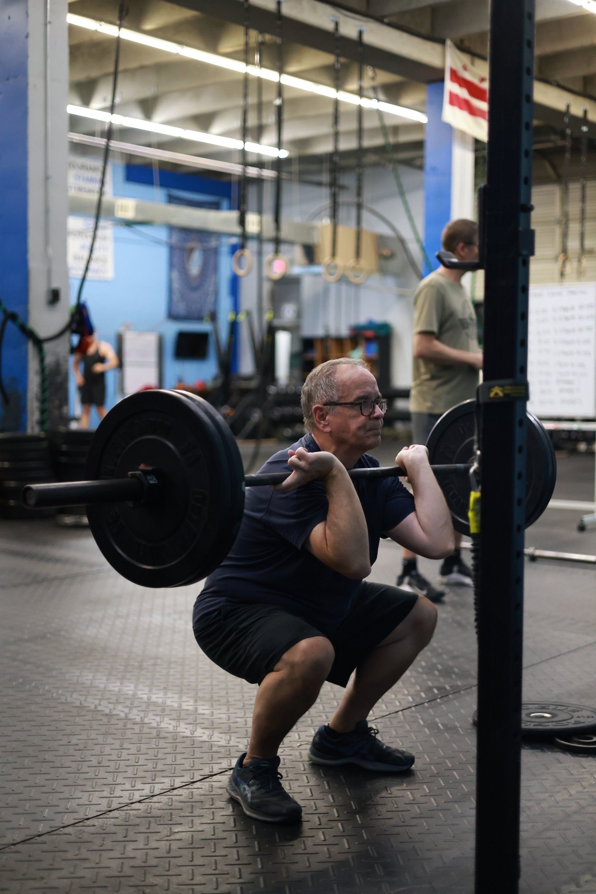 A man is squatting with a barbell on his shoulders in a gym.
