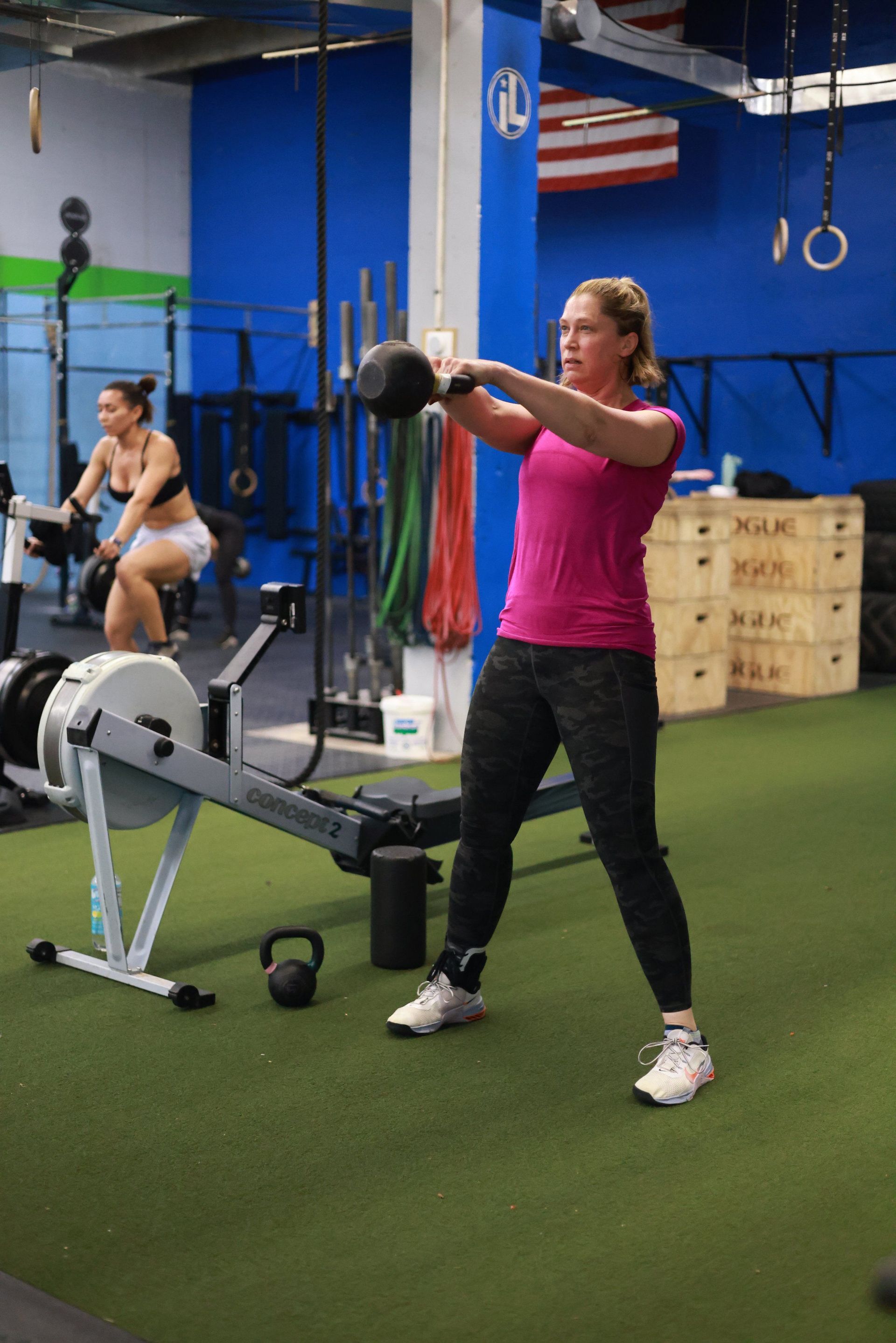 A woman is swinging a kettlebell in a gym.