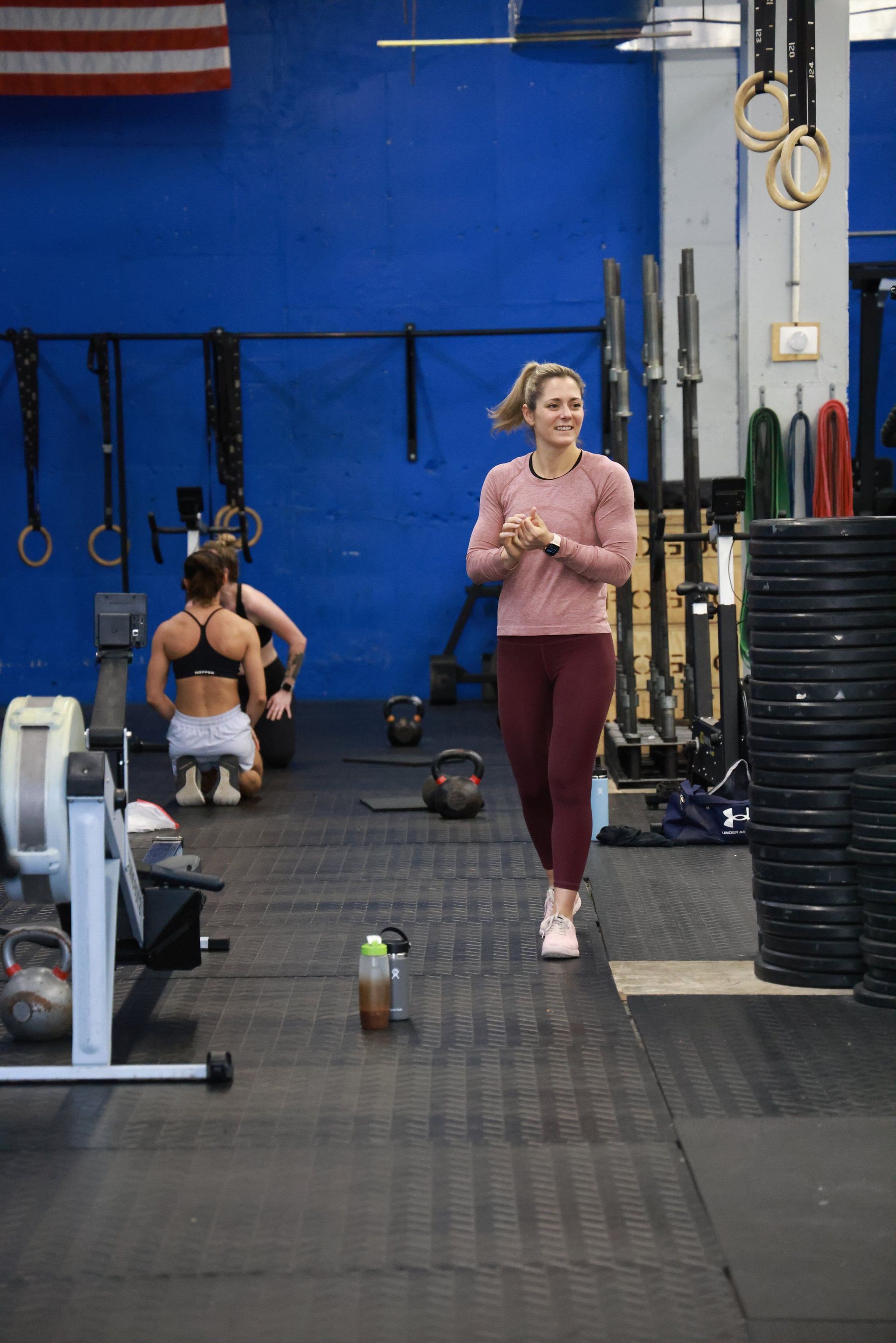 A woman is walking through a gym with people sitting on the floor.