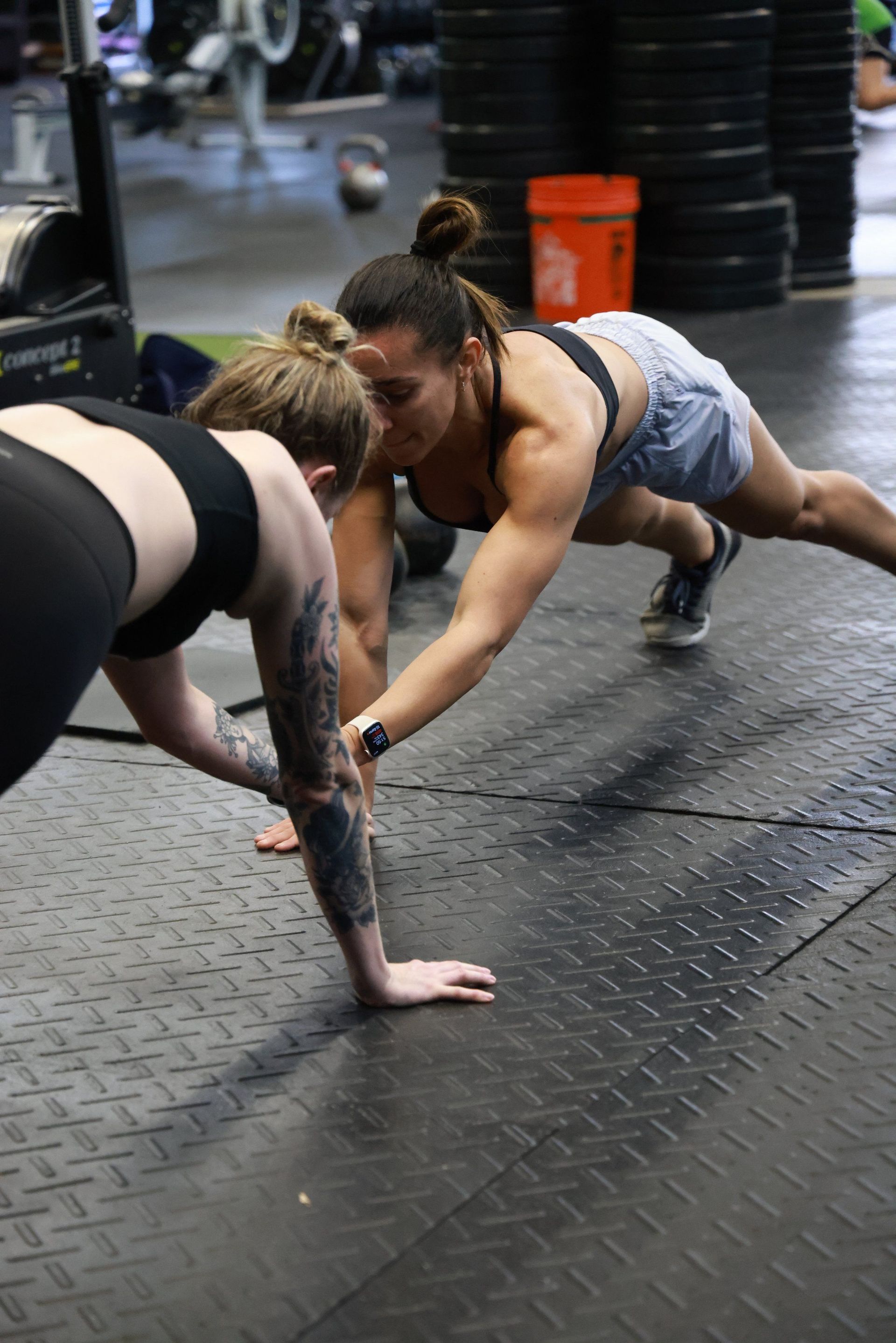 Two women are doing push ups on the floor in a gym.