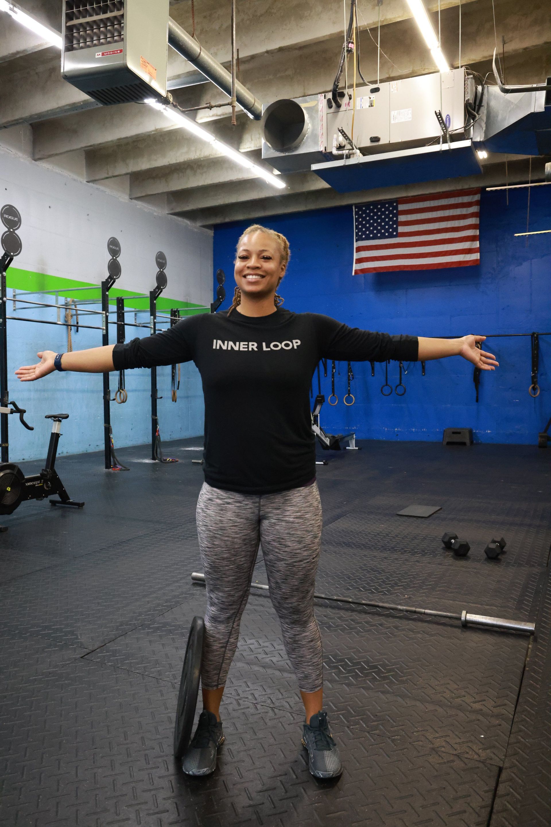 A woman is standing in a gym with her arms outstretched.