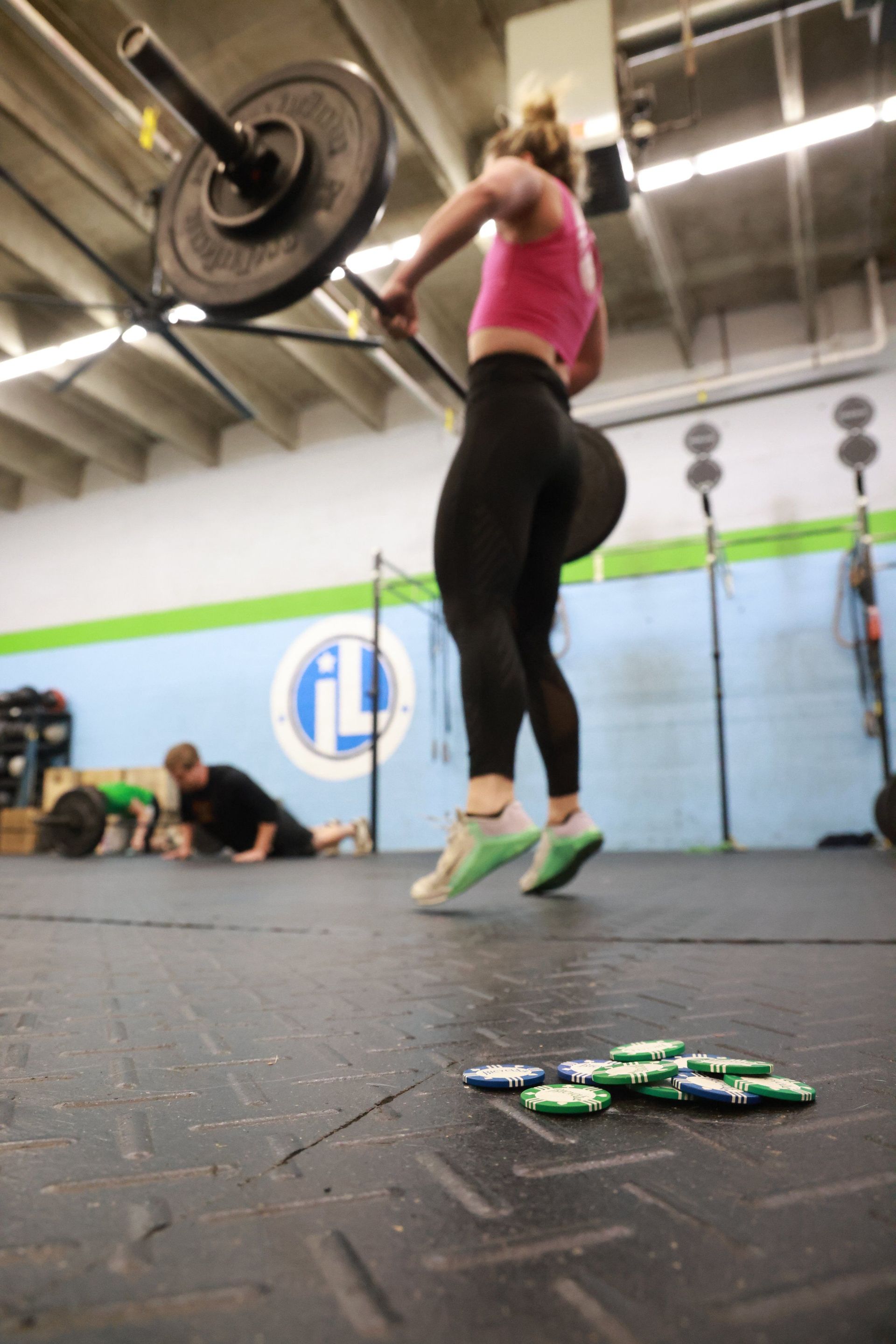 A woman is jumping in the air while lifting a barbell in a gym.