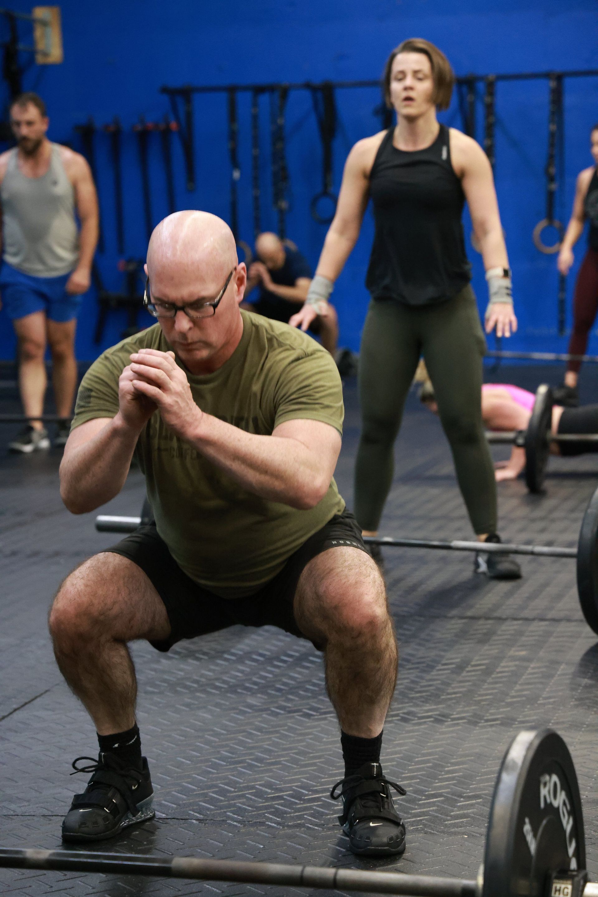 A man is squatting down with a barbell in a gym.