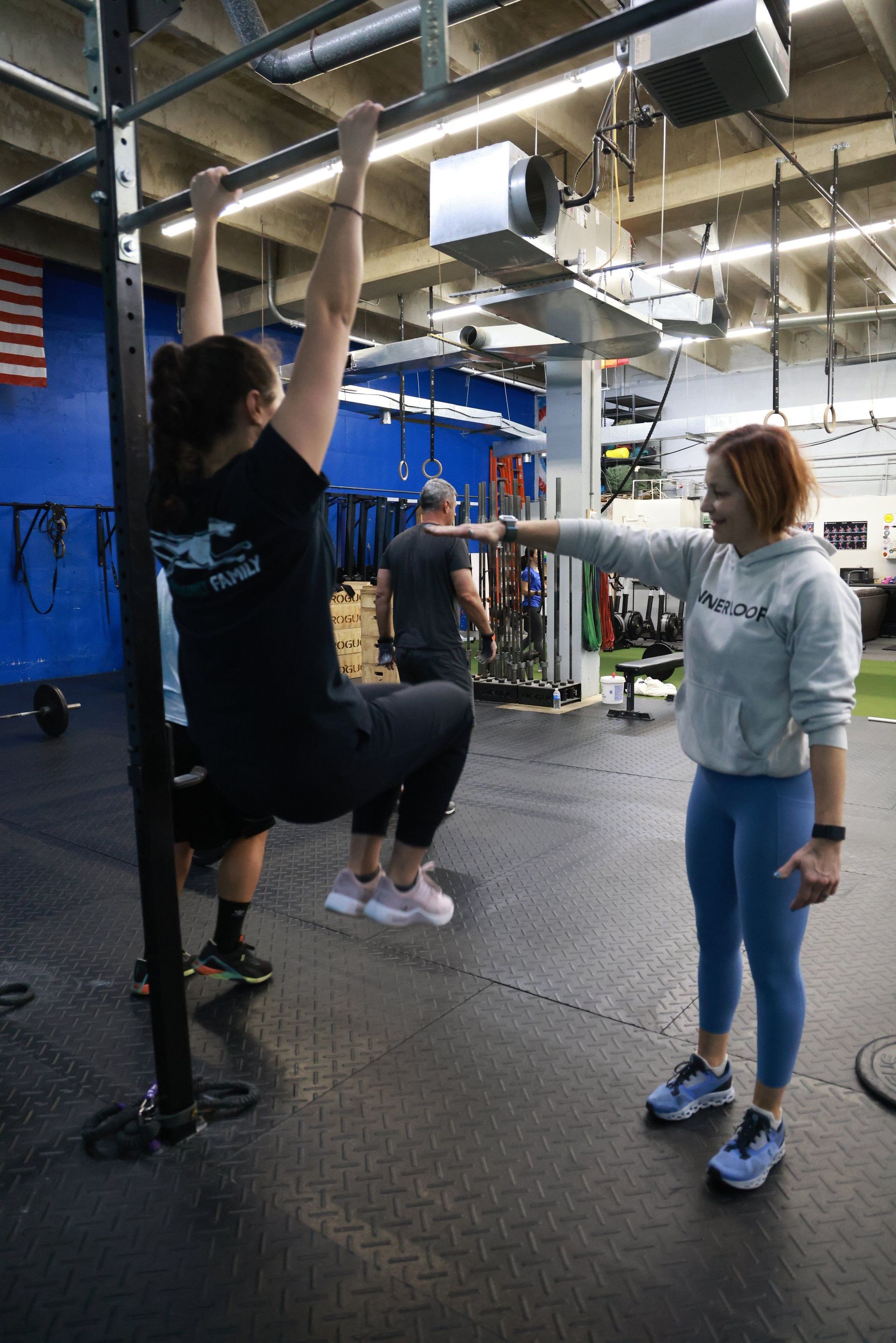 A woman is helping a man do a pull up in a gym.