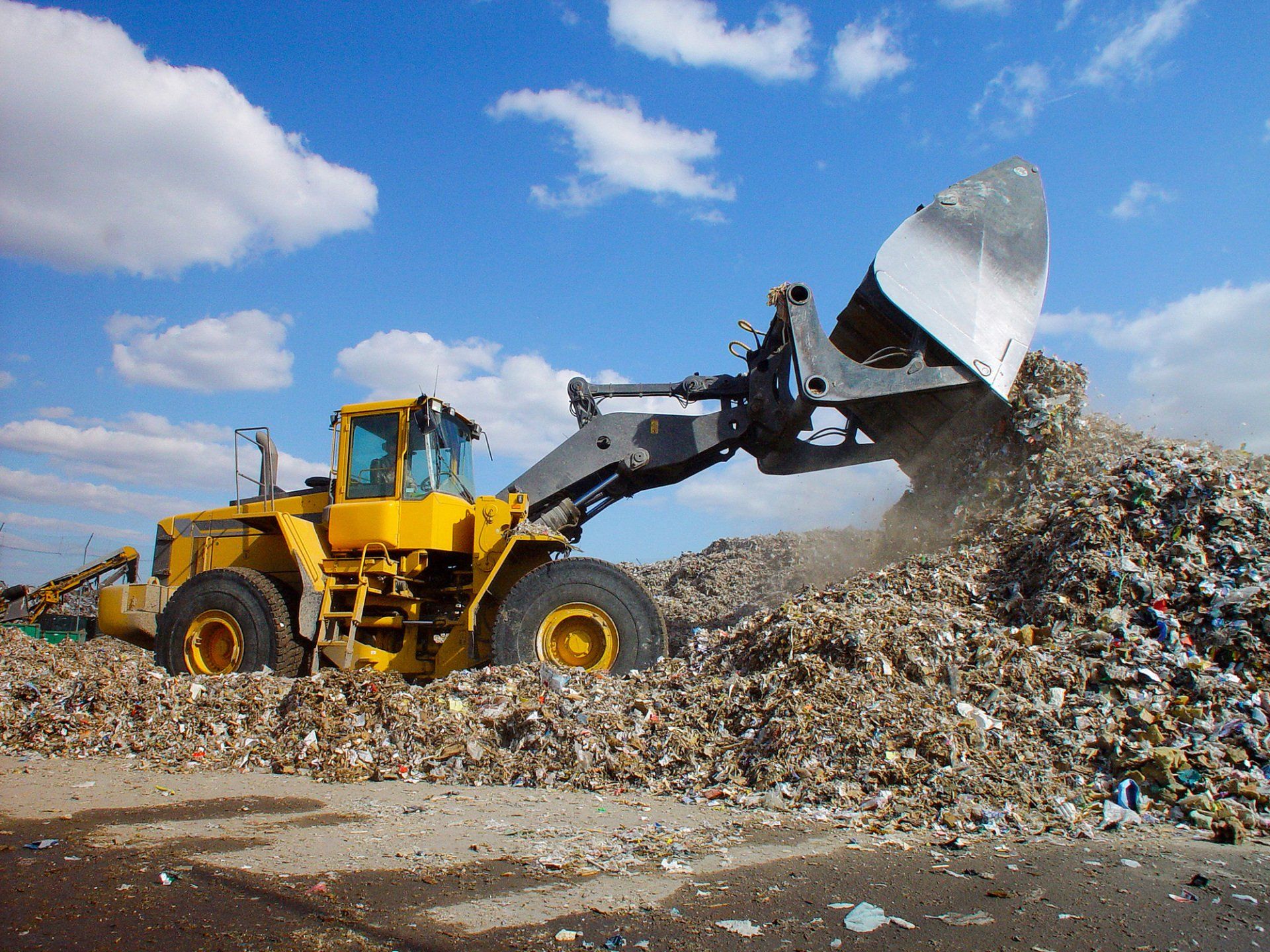 Shot of a loader moving garbage onto a landfill site. Dust from rubbish in air. Plastic bin bags, cardboard and wood visible amongst the garbage.