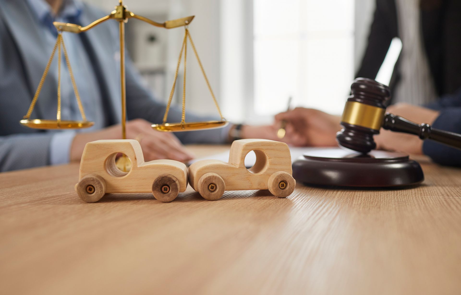 two wood cars running into each other in front of a gavel and scales of justice