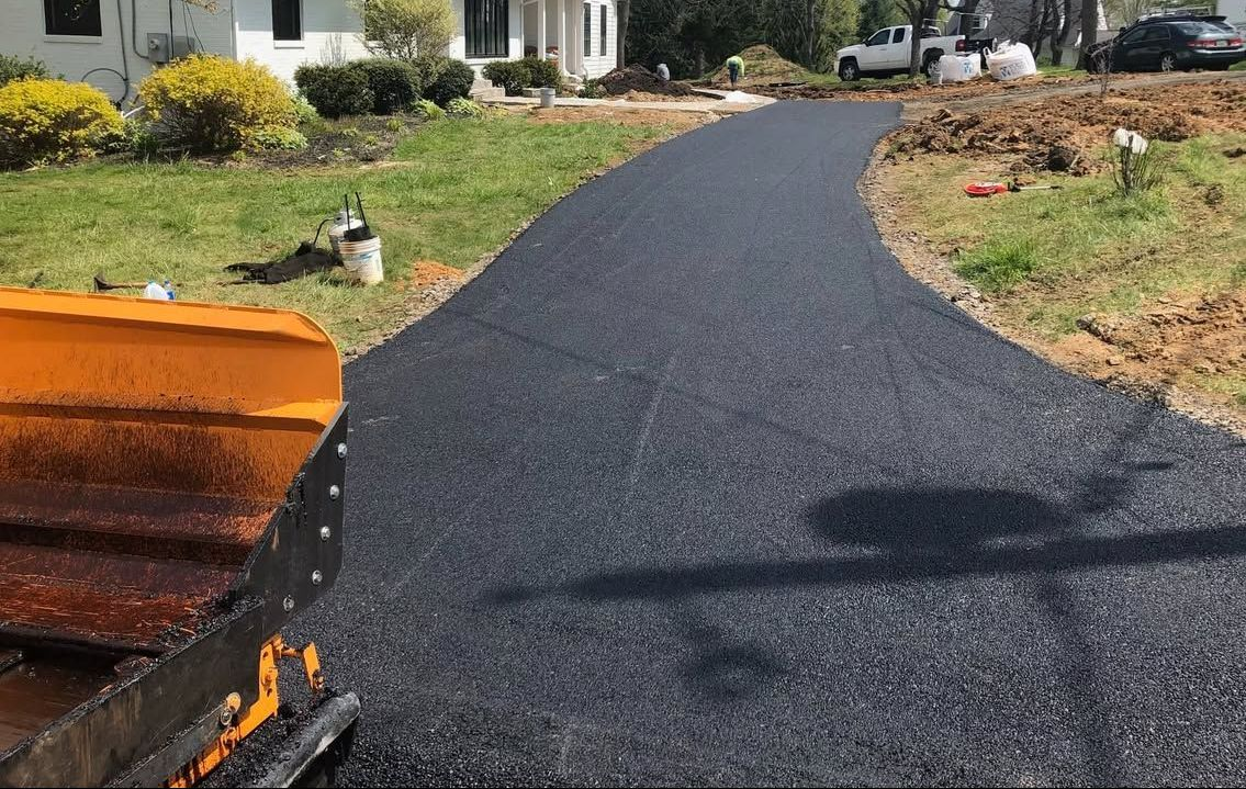 Fresh black asphalt being laid on a curved driveway with a paving machine in the foreground