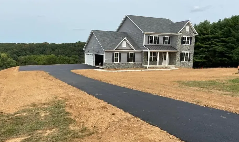 Large gray house with a black driveway on a cleared lot, surrounded by trees
