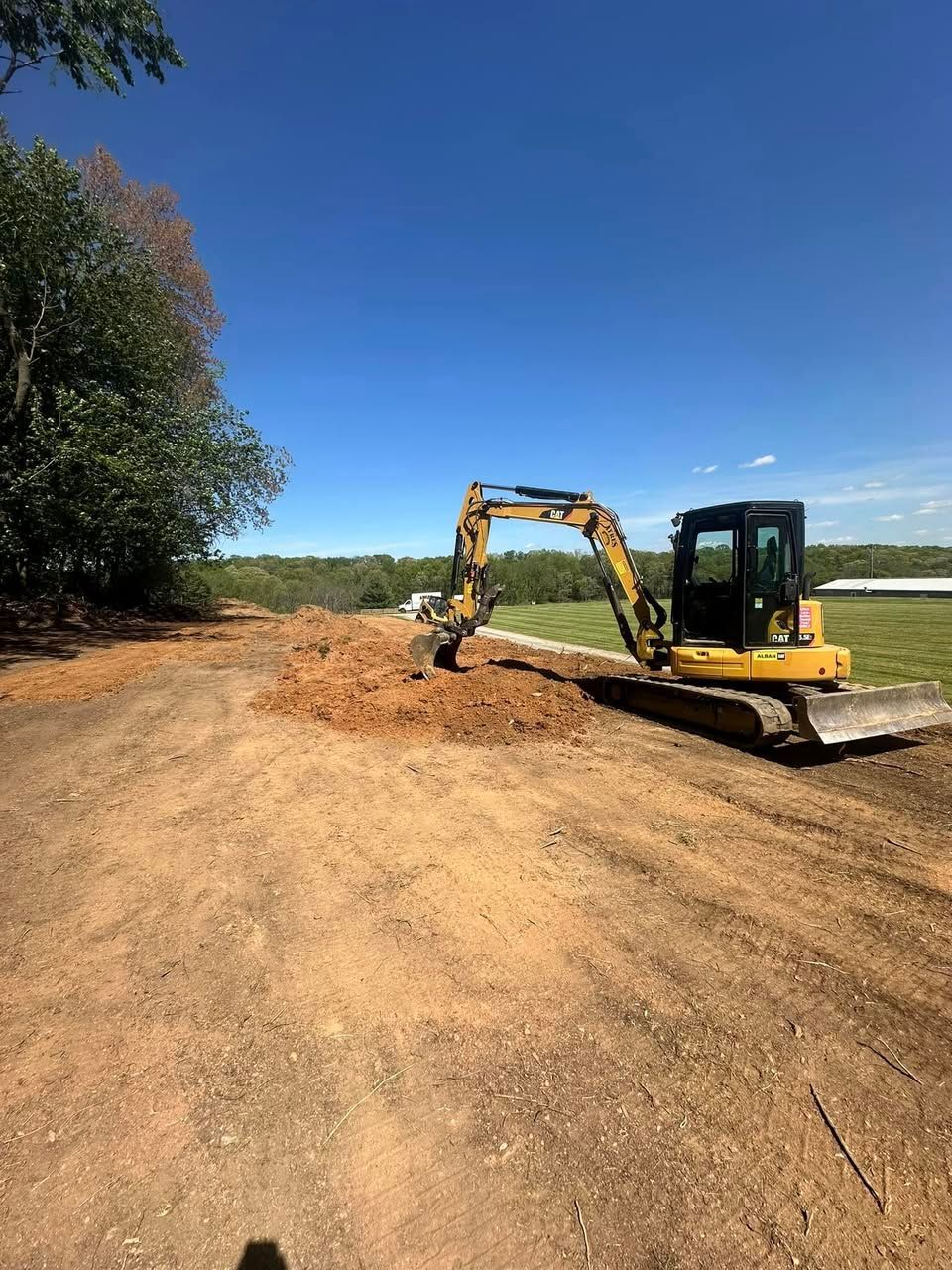 A yellow excavator is digging a hole in the dirt on a dirt road.