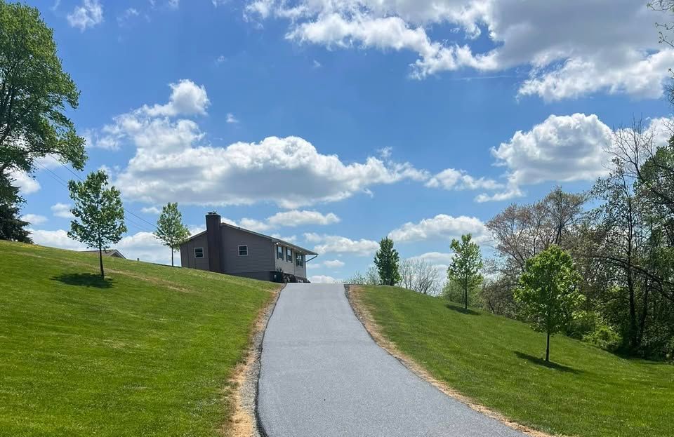A driveway leading to a house on top of a grassy hill.