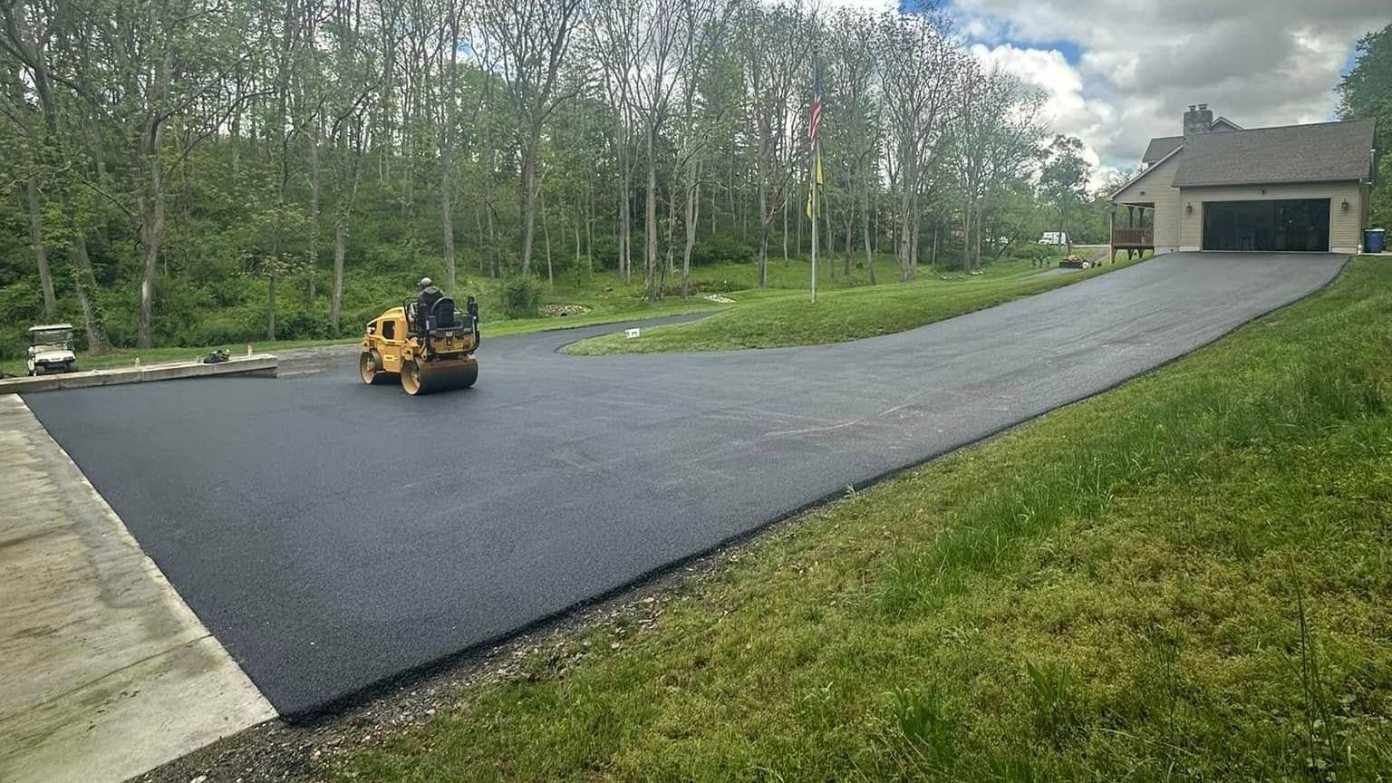 A roller is rolling asphalt on a driveway in front of a house.
