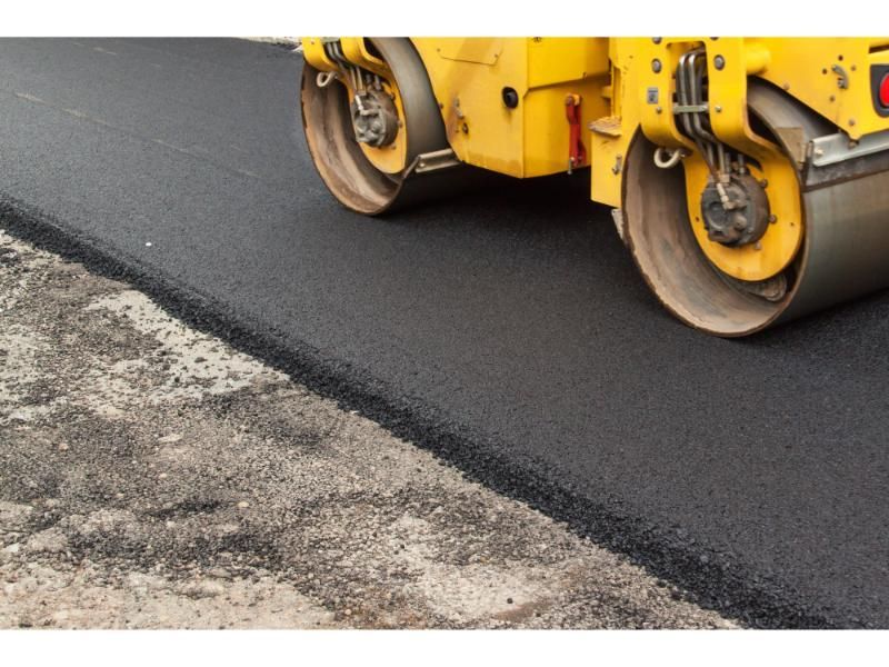 Yellow road roller compacting fresh asphalt on a road.