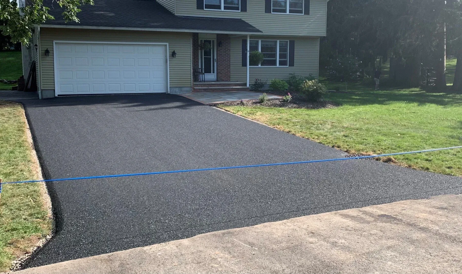 New black asphalt driveway leading to a suburban house with a white garage door