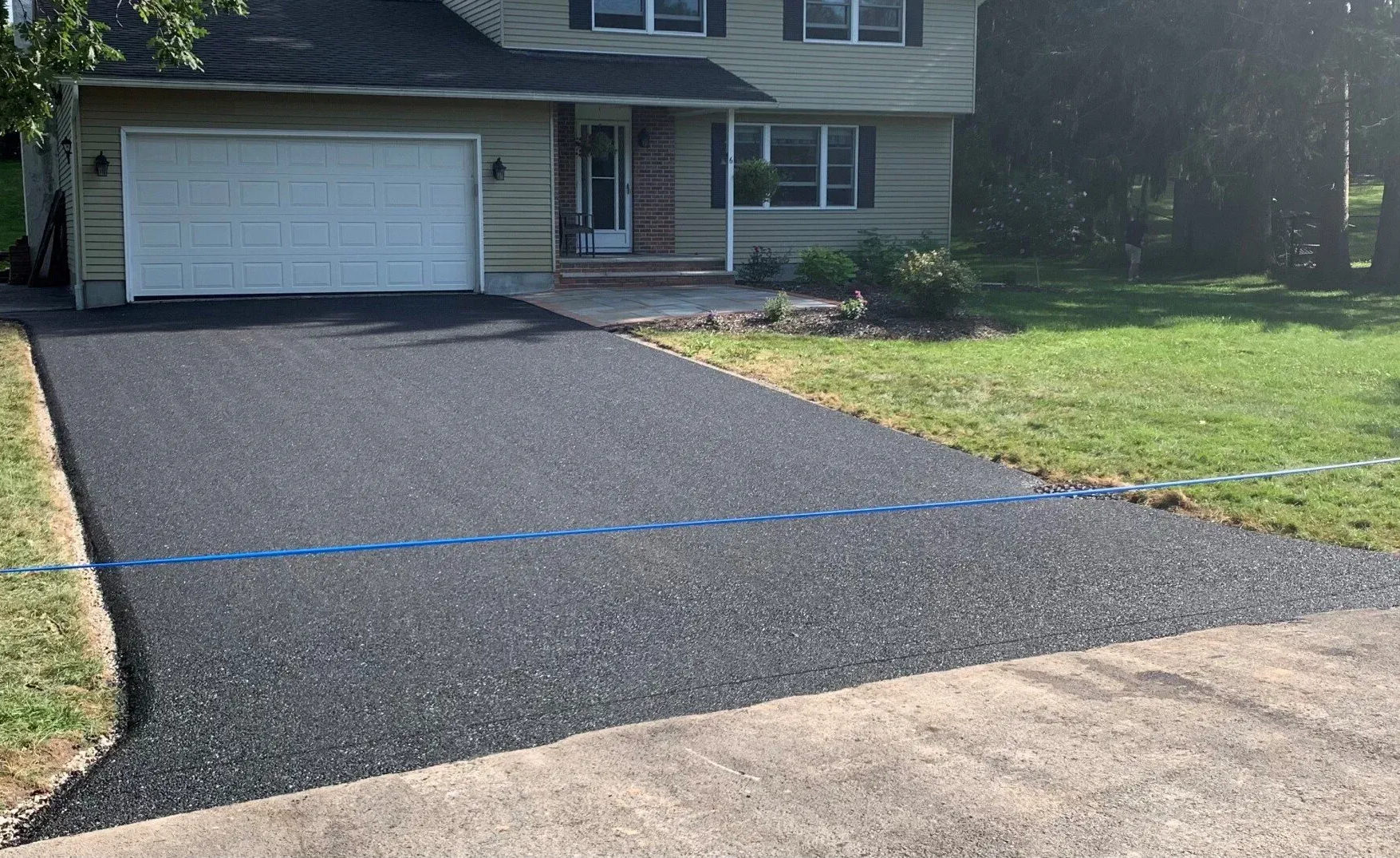 Freshly paved black asphalt driveway leading to a suburban house with a white garage door