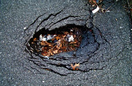 Cracked asphalt with a large pothole filled with leaves and debris