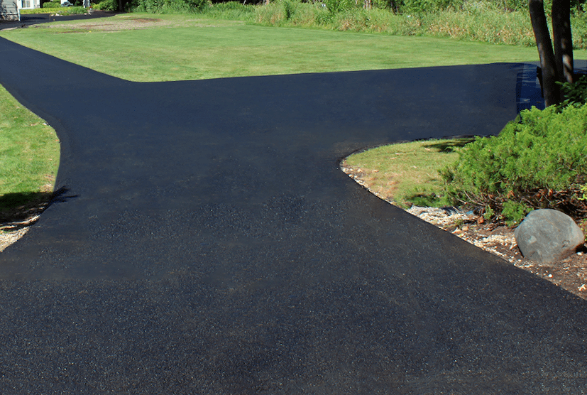 Fresh black asphalt driveway curving through a green lawn with landscaped edging and rocks