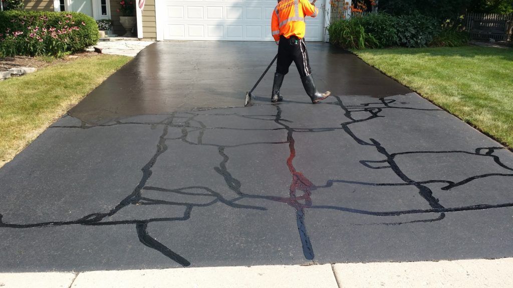 Worker sealing cracks on a driveway with dark crack filler outside a house