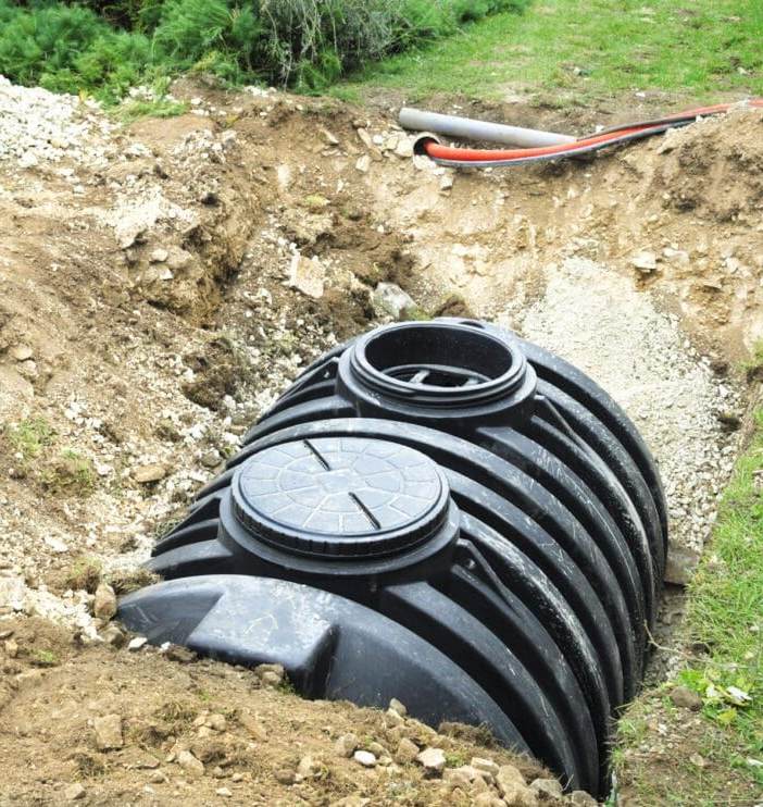 Black, corrugated plastic septic tank in an excavated hole, ready for installation.