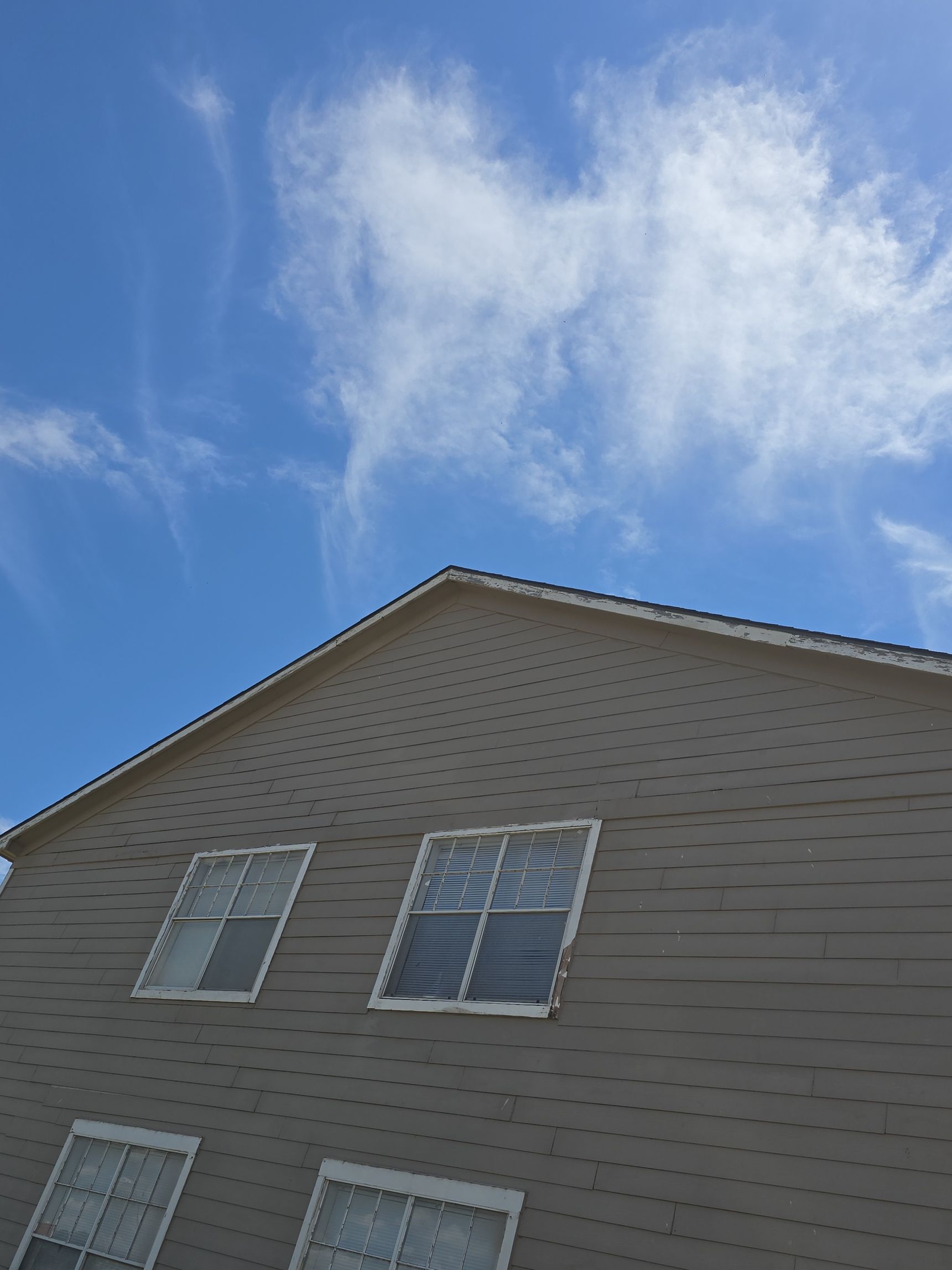 House roof and upper windows against a blue sky with wispy clouds