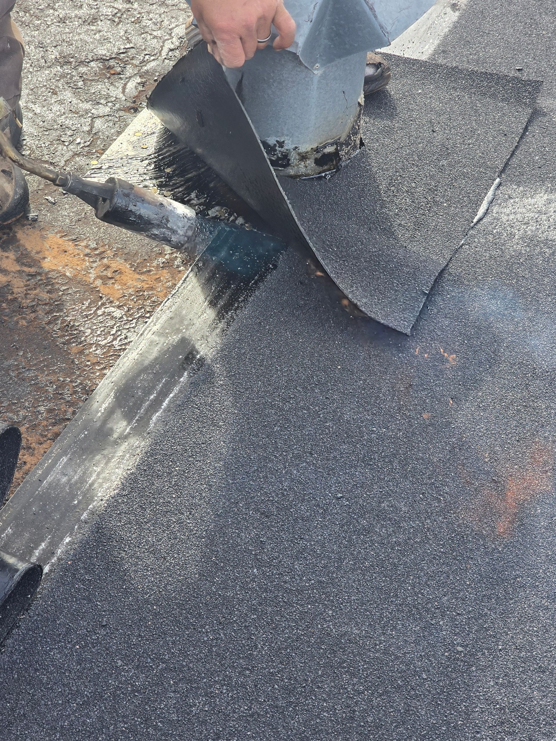 Hands lifting damaged roofing shingles on a dark asphalt roof, exposing a leak area