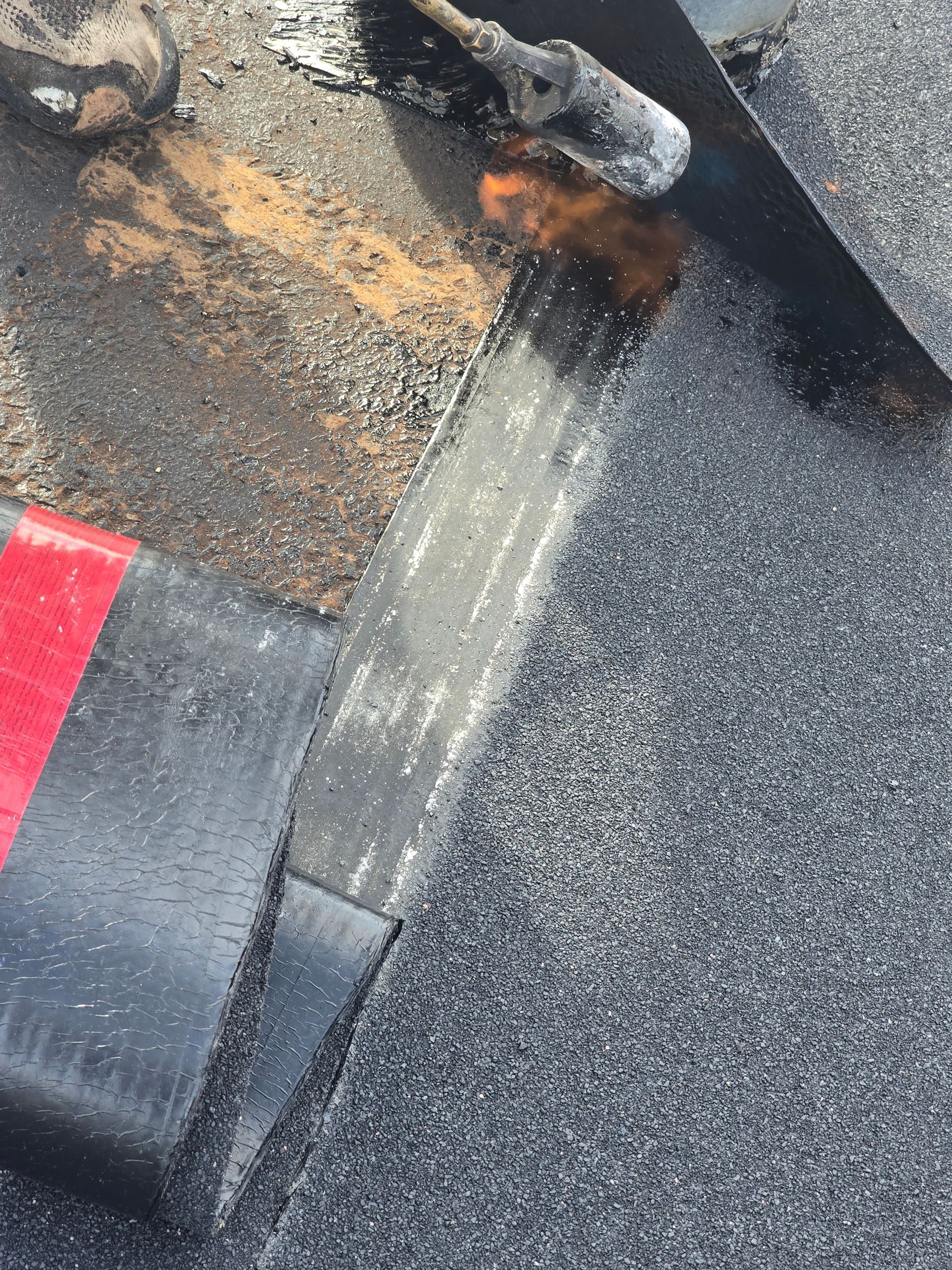 Close-up of damaged asphalt roofing with a worn seam, dark granules, and red flashing visible.