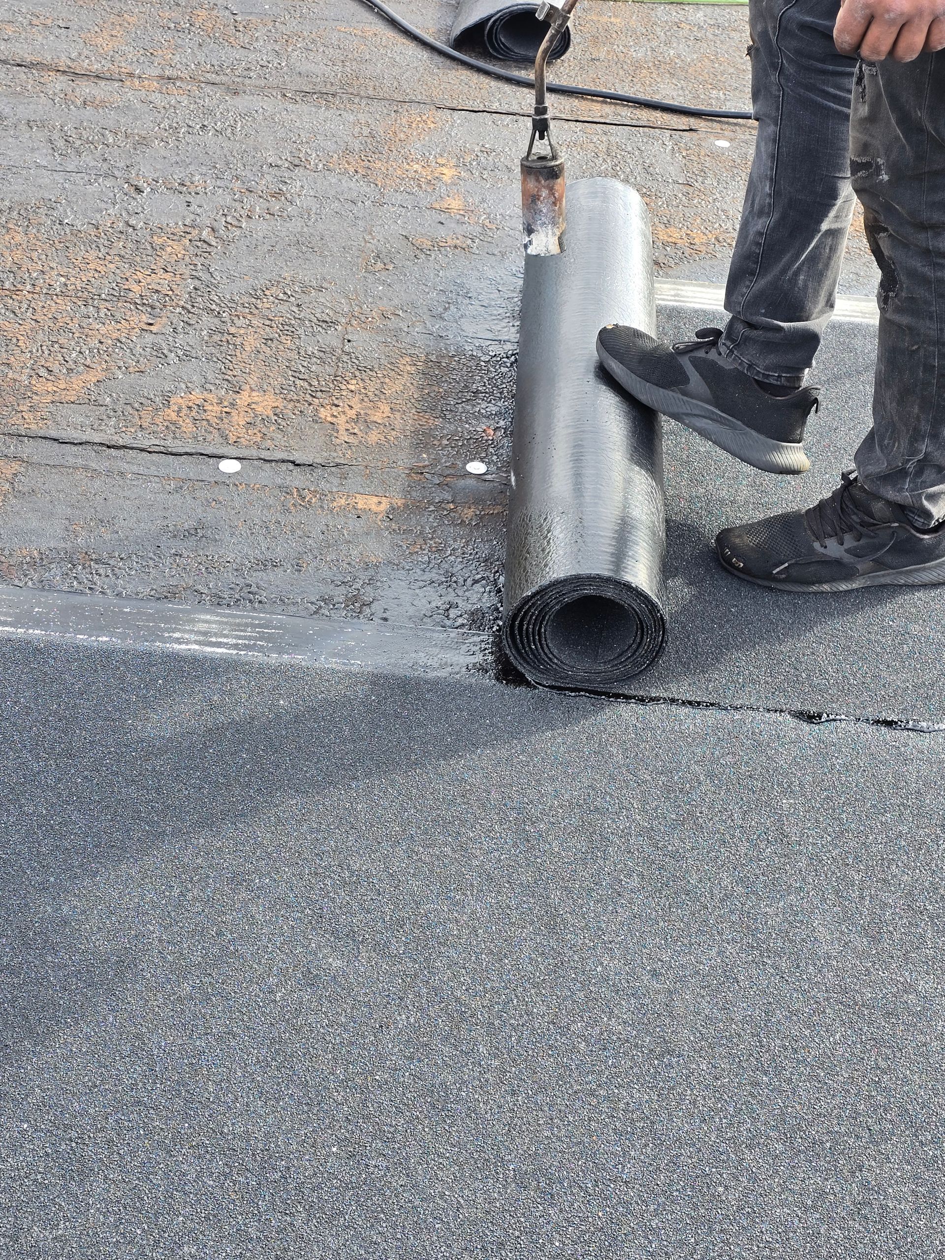 Worker rolling roofing membrane on a flat roof