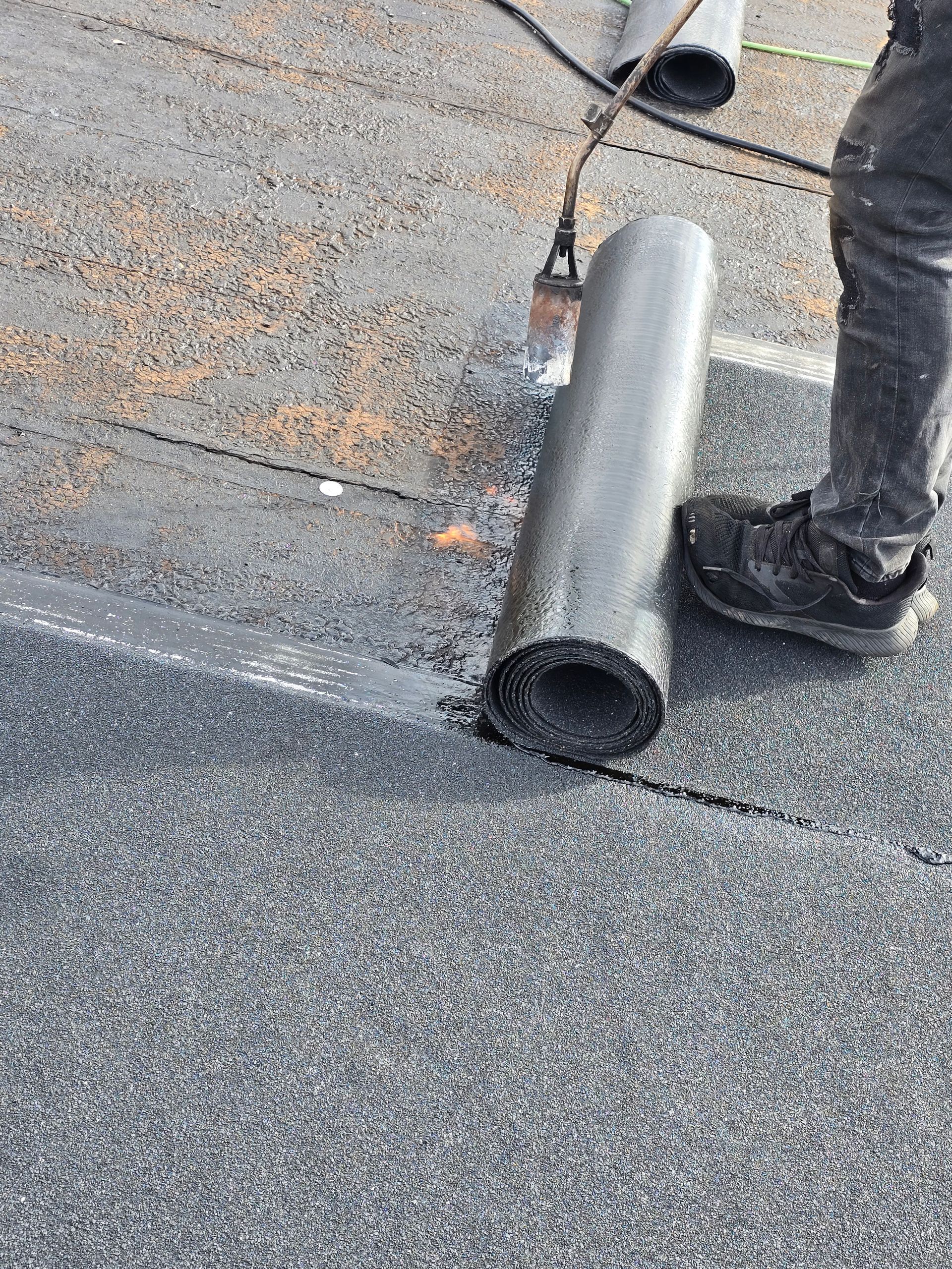 Worker holding a gray metal pipe on a rooftop covered with gravel shingles