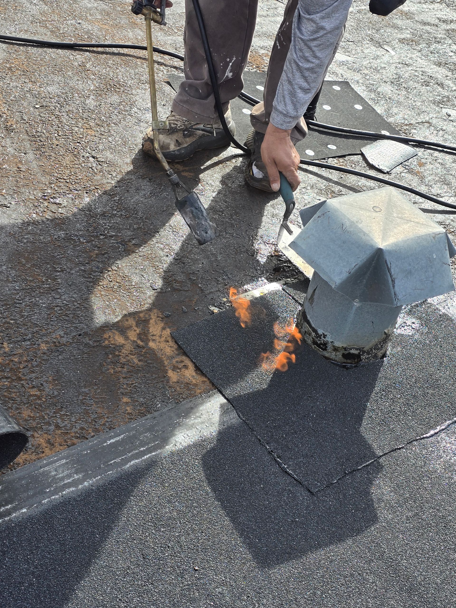 Person inspecting rooftop vent near a gas flame on a gravel-covered roof