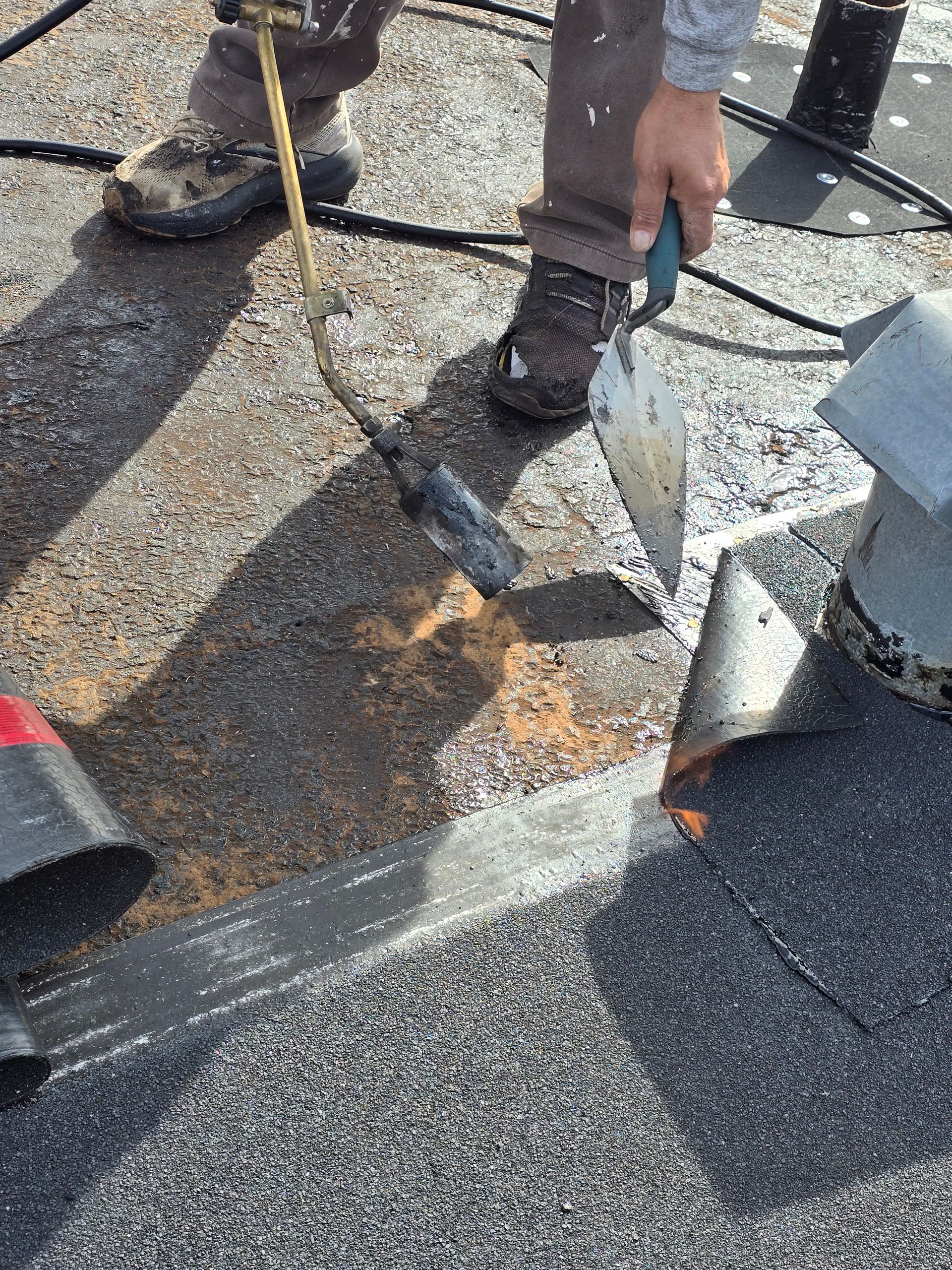 Worker prying up damaged roof shingles with a tool during roof repair