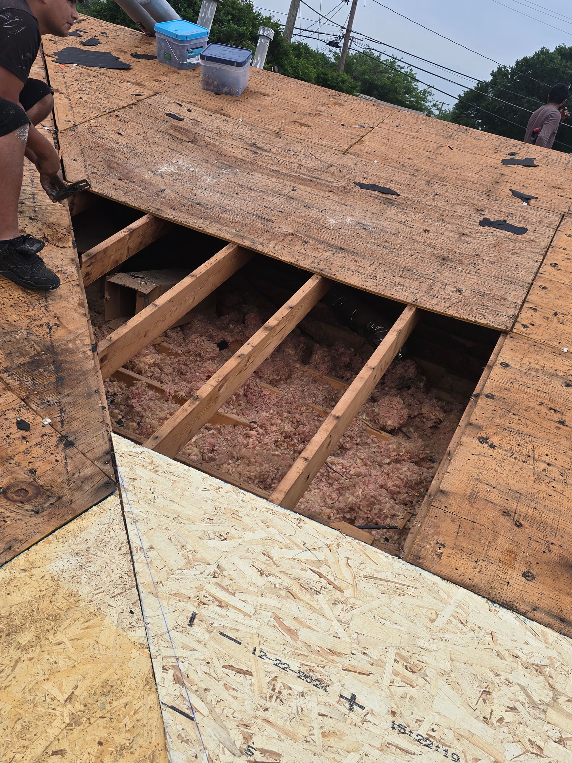 Damaged rooftop with exposed wooden beams and plywood panels under cloudy sky