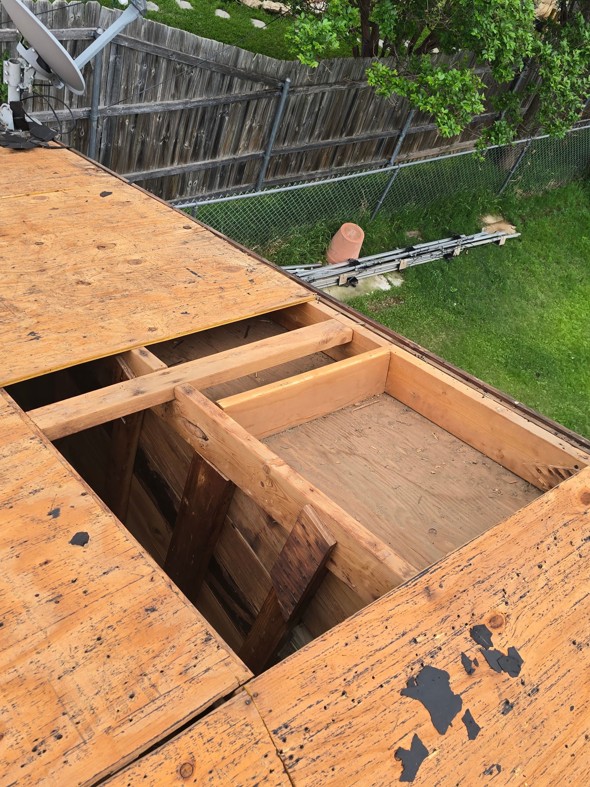 Damaged wooden deck with a large open hole and exposed framing beside a fence