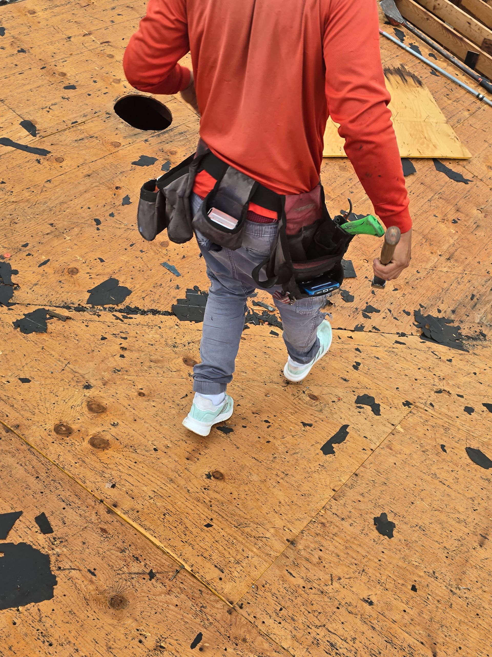 Worker in a red jacket walking across a dirt surface, carrying climbing gear and a tool pouch.