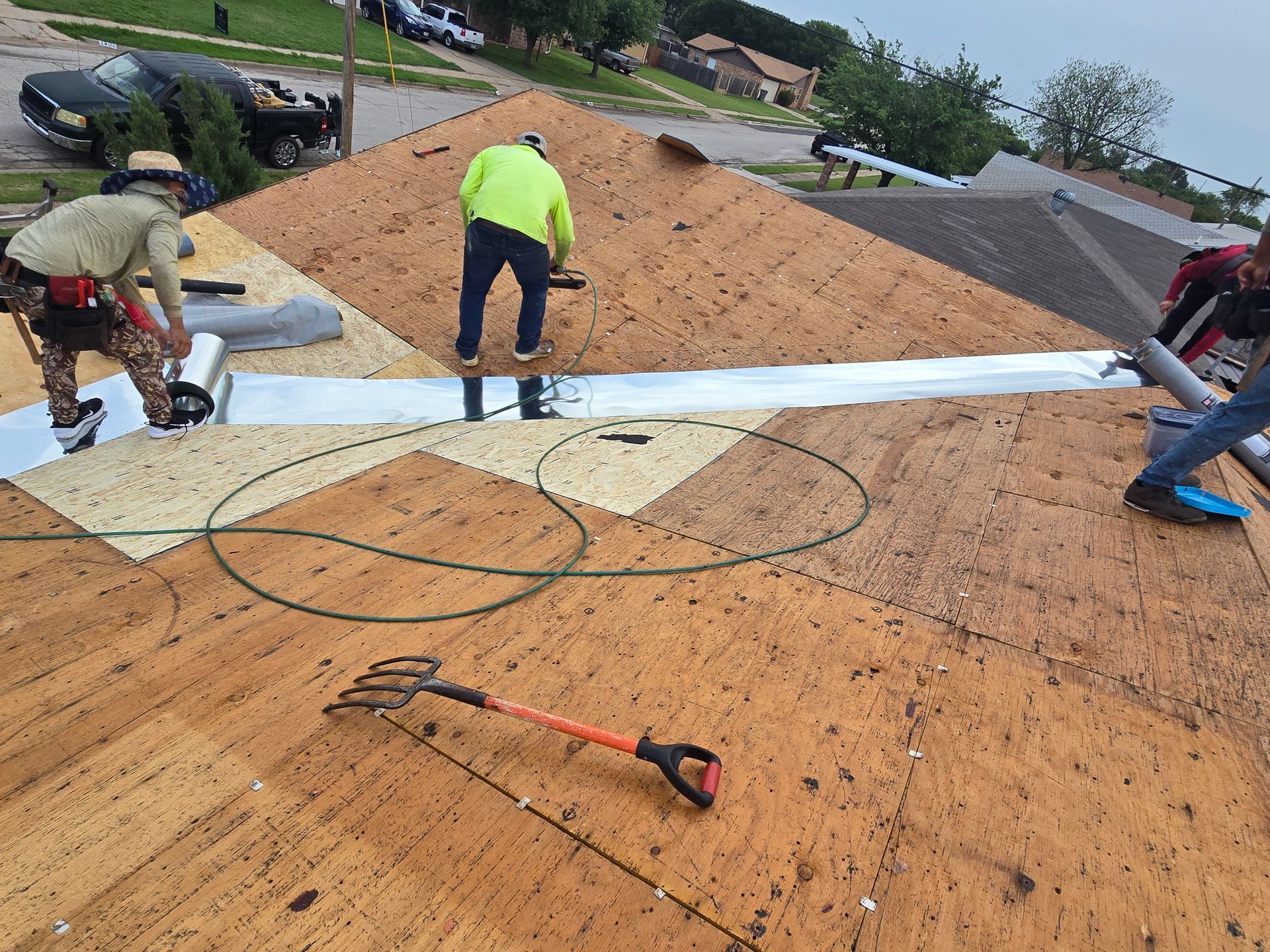 Workers installing a roof membrane on a sloped roof with tools and white panels